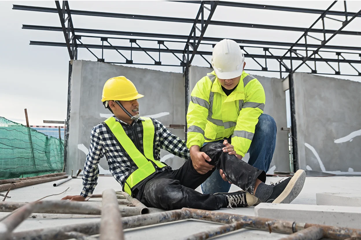 An injured construction worker at a job site being helped by a co-worker